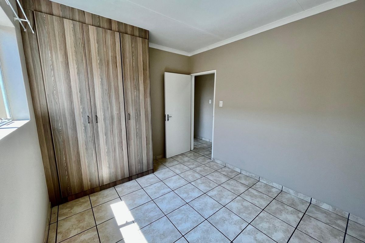 A clean, empty bedroom featuring neutral wall tones, durable tiled flooring, and ample built-in cupboard storage space.