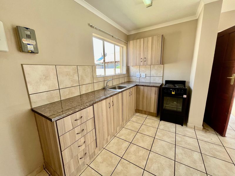 Functional kitchen featuring laminate cabinetry, granite-look countertops, stainless steel sink, and tiled flooring. Includes a freestanding oven and hob.