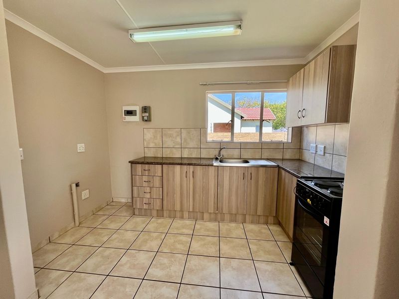 A functional kitchen featuring laminate cabinetry, granite countertops, tiled backsplash, and ceramic floor tiles, equipped with a freestanding stove and stainless steel sink.