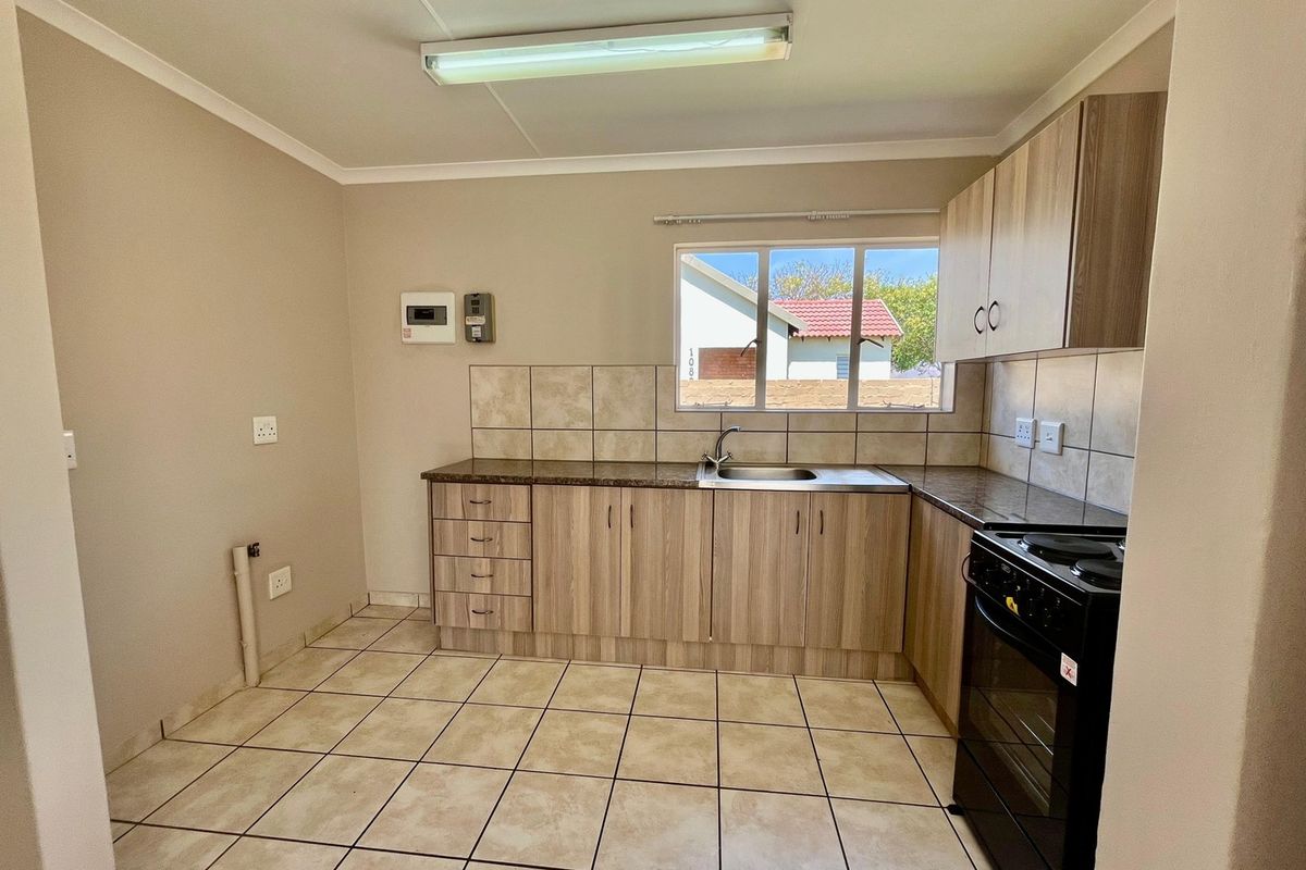 A functional kitchen featuring laminate cabinetry, granite countertops, tiled backsplash, and ceramic floor tiles, equipped with a freestanding stove and stainless steel sink.