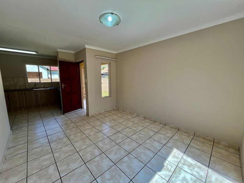 An open-plan living and kitchen area featuring neutral tiled flooring, built-in kitchen cabinetry, and direct access to the exterior.