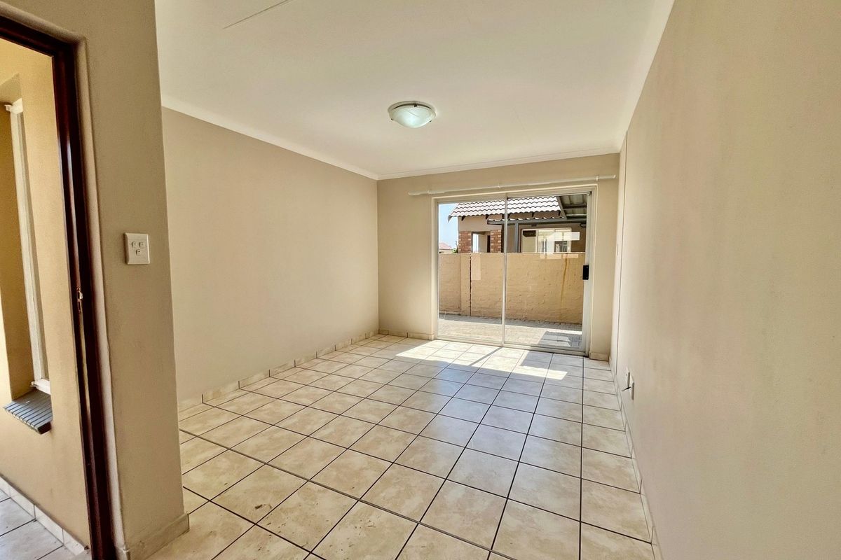 An empty living room featuring neutral walls, tiled flooring, and a sliding glass door providing access to the exterior patio area.