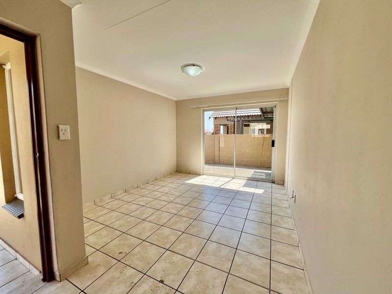 An empty living room featuring neutral walls, tiled flooring, and a sliding glass door providing access to the exterior patio area.