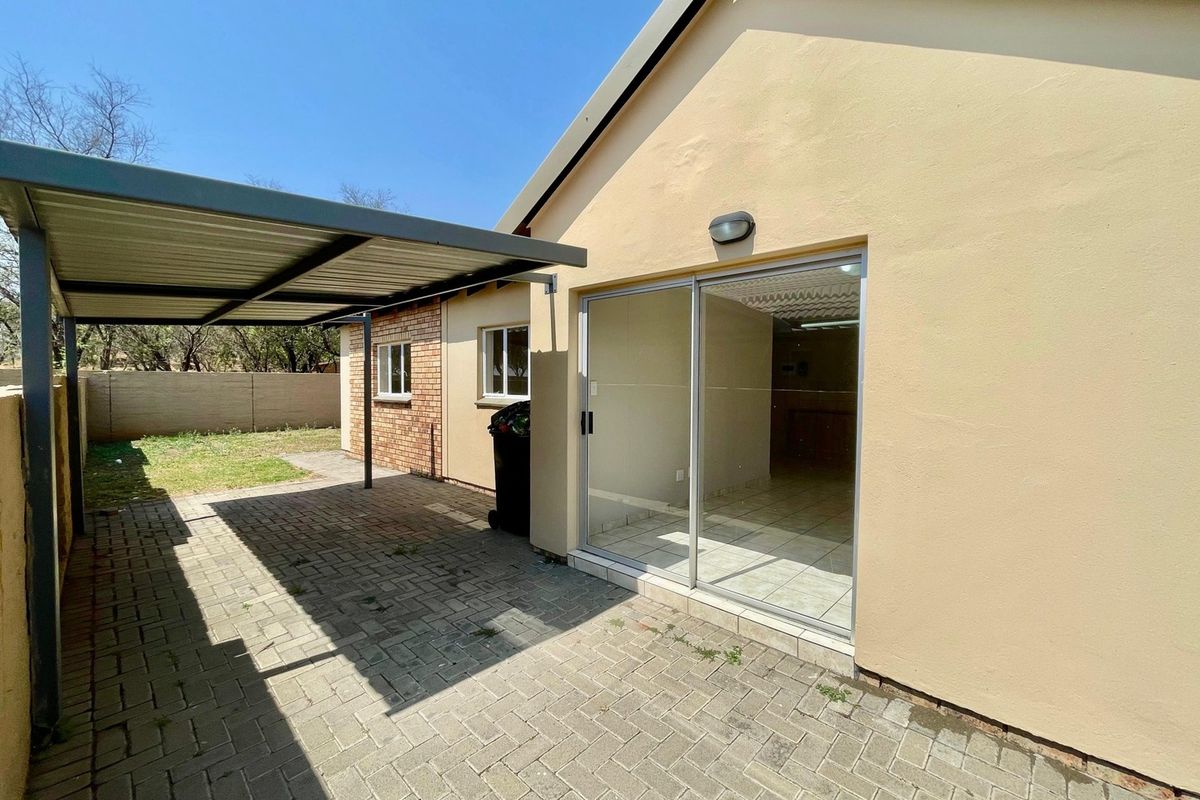 Rear exterior view of the townhouse featuring a paved patio area, a covered carport, and a sliding glass door entrance.