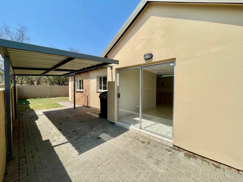 Rear exterior view of the townhouse featuring a paved patio area, a covered carport, and a sliding glass door entrance.