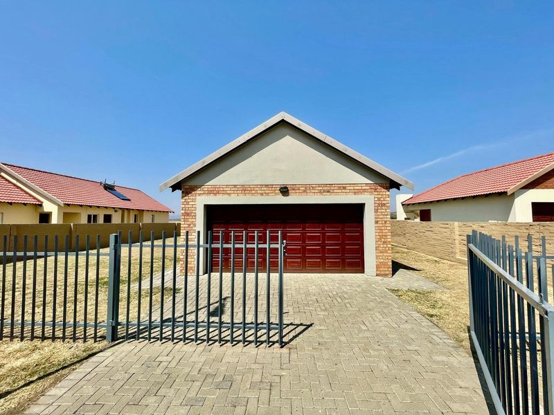 A detached brick garage with a sectional door, featuring a paved driveway and secure steel perimeter fencing in a residential townhouse complex.