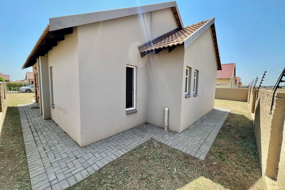 Rear view of the townhouse featuring a paved walkway, tiled roof, and perimeter wall with electric fencing.