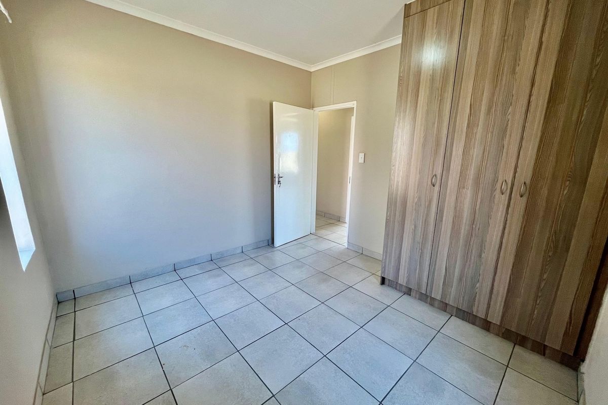 A clean, empty bedroom featuring neutral wall tones, tiled flooring, and ample built-in wooden cupboards.
