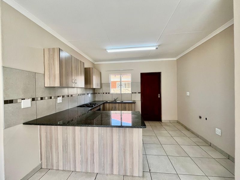 A clean, modern kitchen featuring granite countertops, wood-finish cabinetry, a gas hob, and tiled flooring in an open-plan layout.