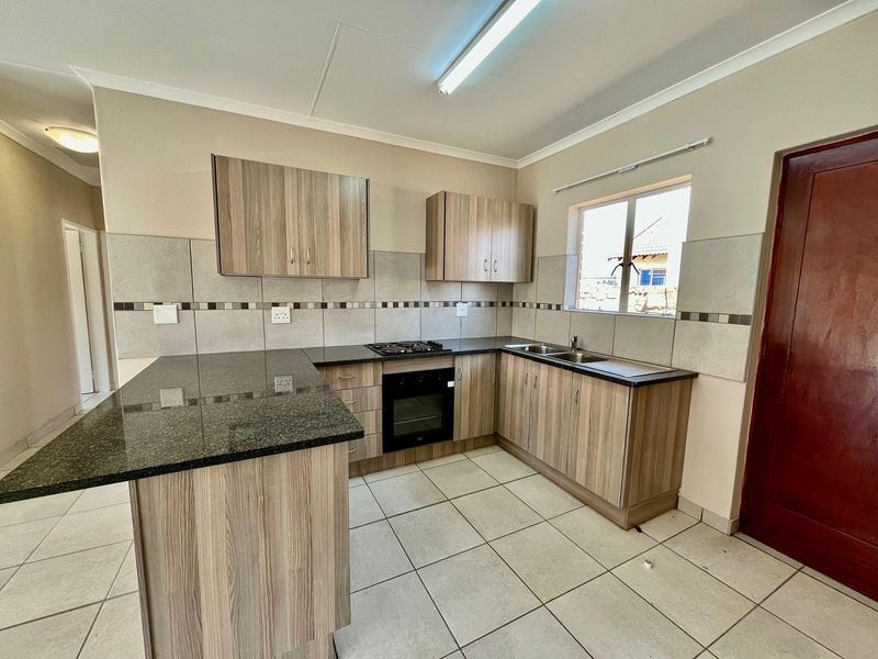 A clean, functional kitchen featuring granite countertops, built-in oven, gas hob, and ample laminate cabinetry with a tiled backsplash.