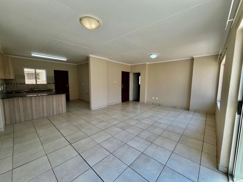 Spacious open-plan living area featuring tiled flooring, neutral walls, and an integrated kitchen with built-in cabinetry and stove, offering a versatile layout.