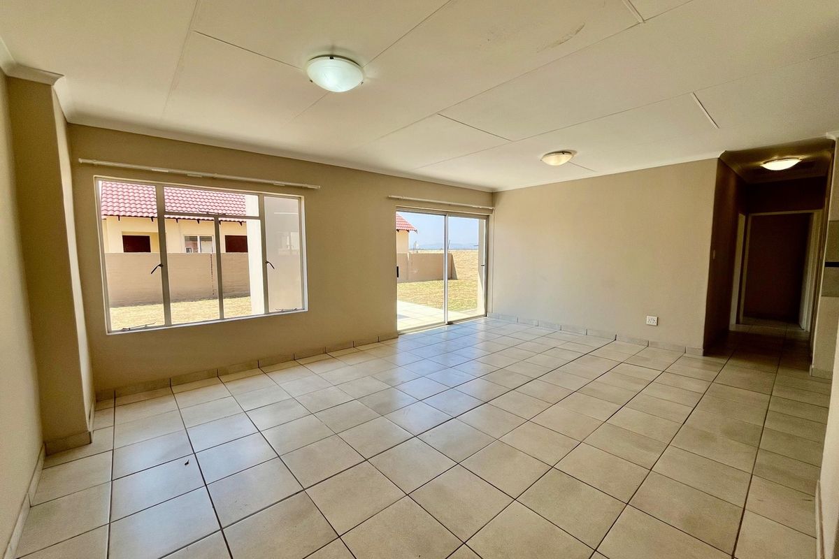 Spacious, empty living area featuring neutral tiled flooring, large windows, and sliding door access to the rear garden.