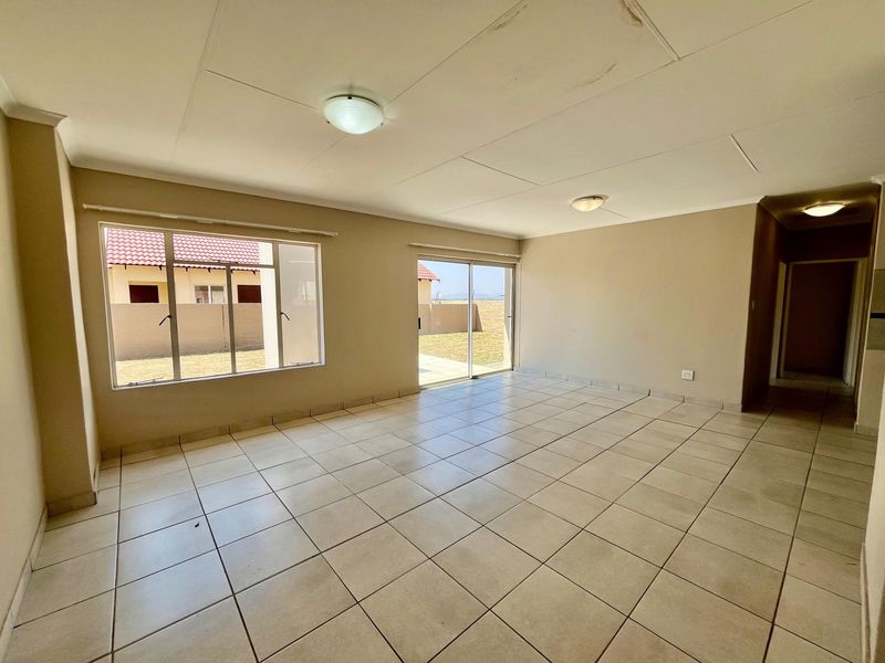 Spacious, empty living area featuring neutral tiled flooring, large windows, and sliding door access to the rear garden.