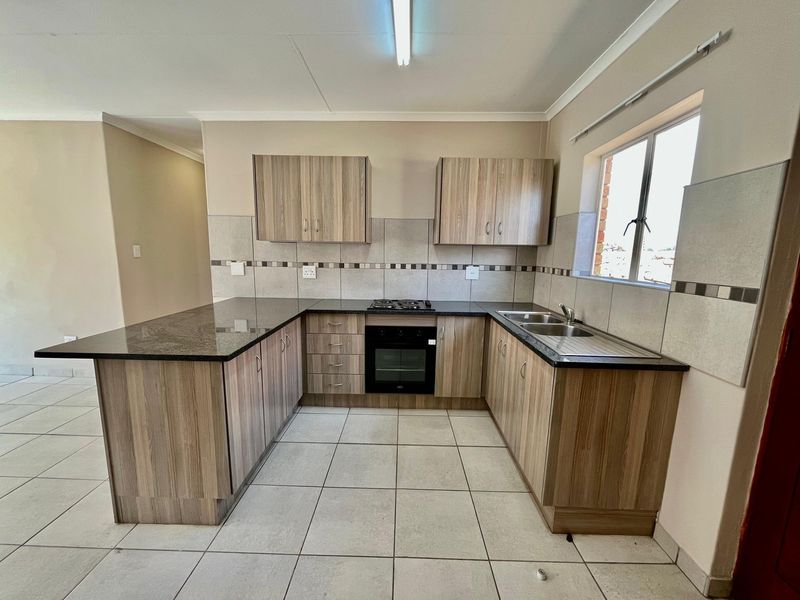 A clean, modern kitchen featuring wood-finish cabinetry, granite countertops, a built-in oven, gas hob, and tiled flooring in an open-plan layout.