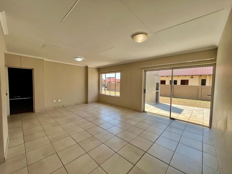 An empty, open-plan living area featuring neutral tiled flooring, ceiling lighting, and large sliding glass doors providing direct access to the rear patio and garden.