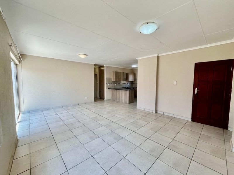 Spacious open-plan living area featuring neutral tiled flooring, a functional kitchen with built-in cabinetry, and direct access to an outdoor space via sliding doors.