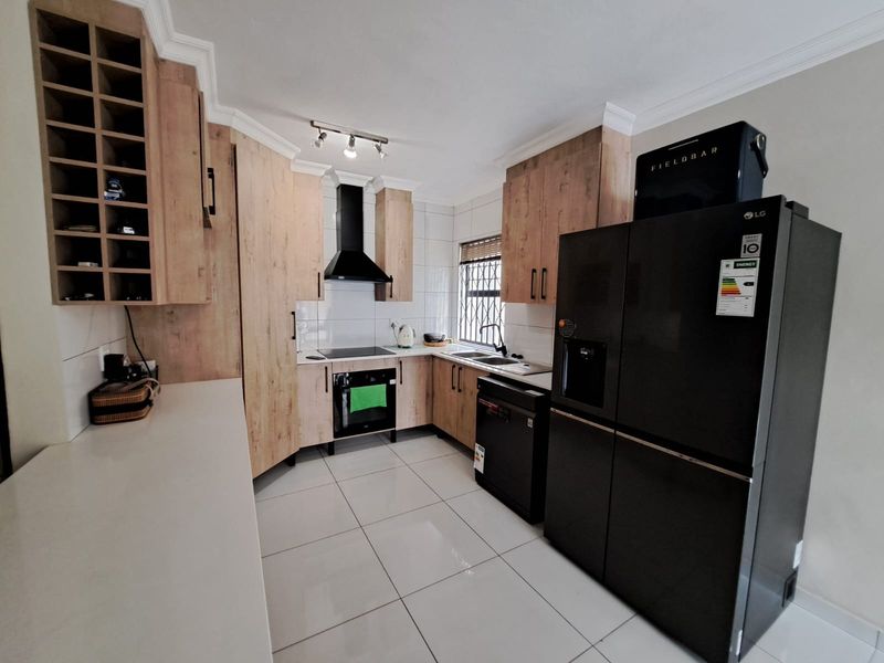 Modern kitchen featuring light wood-finish cabinetry, tiled flooring, built-in oven, electric hob, and a dedicated wine rack for convenient storage.