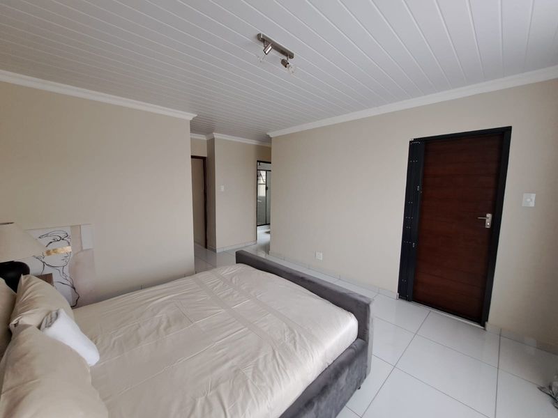 A well-maintained bedroom featuring neutral wall tones, tiled flooring, and a white tongue and groove ceiling with a modern light fixture.