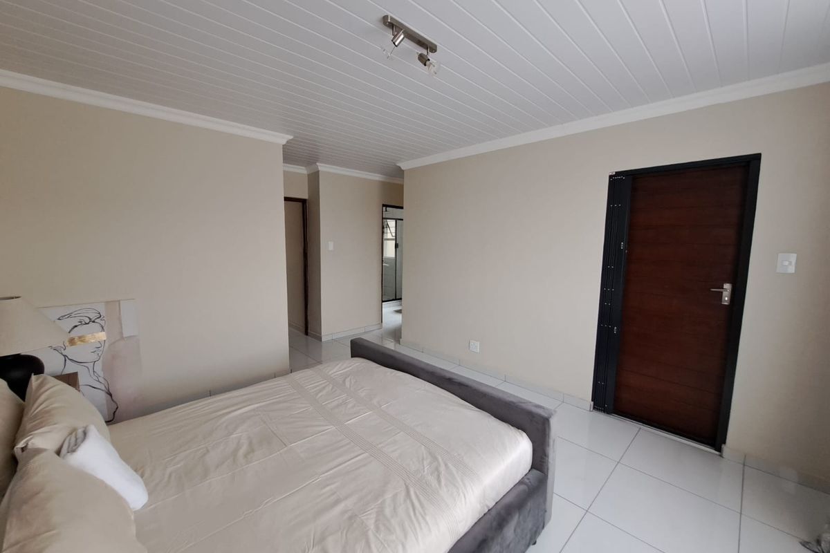 A well-maintained bedroom featuring neutral wall tones, tiled flooring, and a white tongue and groove ceiling with a modern light fixture.