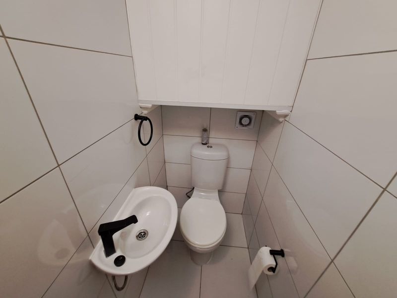 A compact, modern guest bathroom featuring white wall tiles, a wall-mounted basin with black tapware, and a standard toilet.