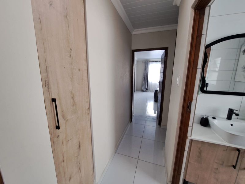 A clean, tiled hallway featuring a built-in cupboard and access to an adjacent bathroom with a modern vanity and basin.
