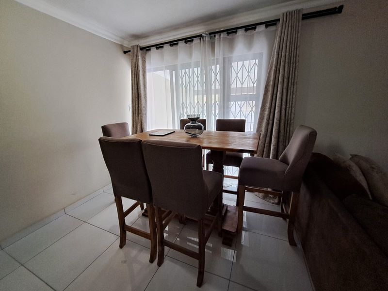 A dining area featuring tiled flooring and a large window fitted with a security gate and curtains.