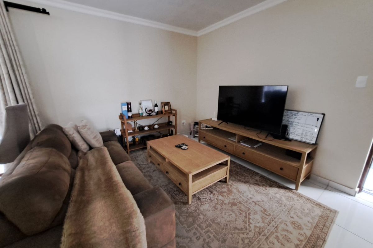 A comfortable living room featuring neutral walls, tiled flooring, and decorative cove cornicing, providing a functional and well-lit space for relaxation.