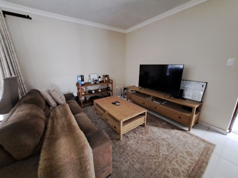 A comfortable living room featuring neutral walls, tiled flooring, and decorative cove cornicing, providing a functional and well-lit space for relaxation.