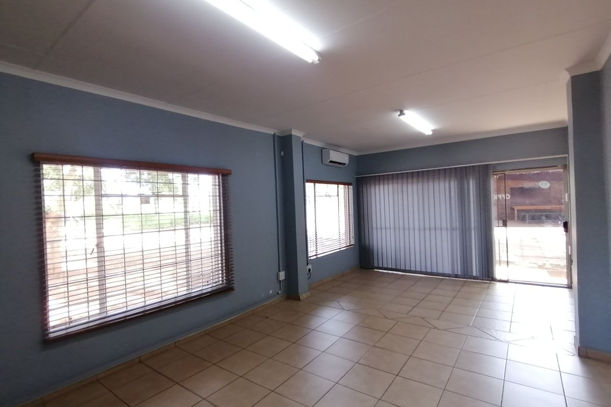A spacious, empty living area featuring tiled floors, air conditioning, and large windows with fitted blinds, offering a bright and versatile interior space.
