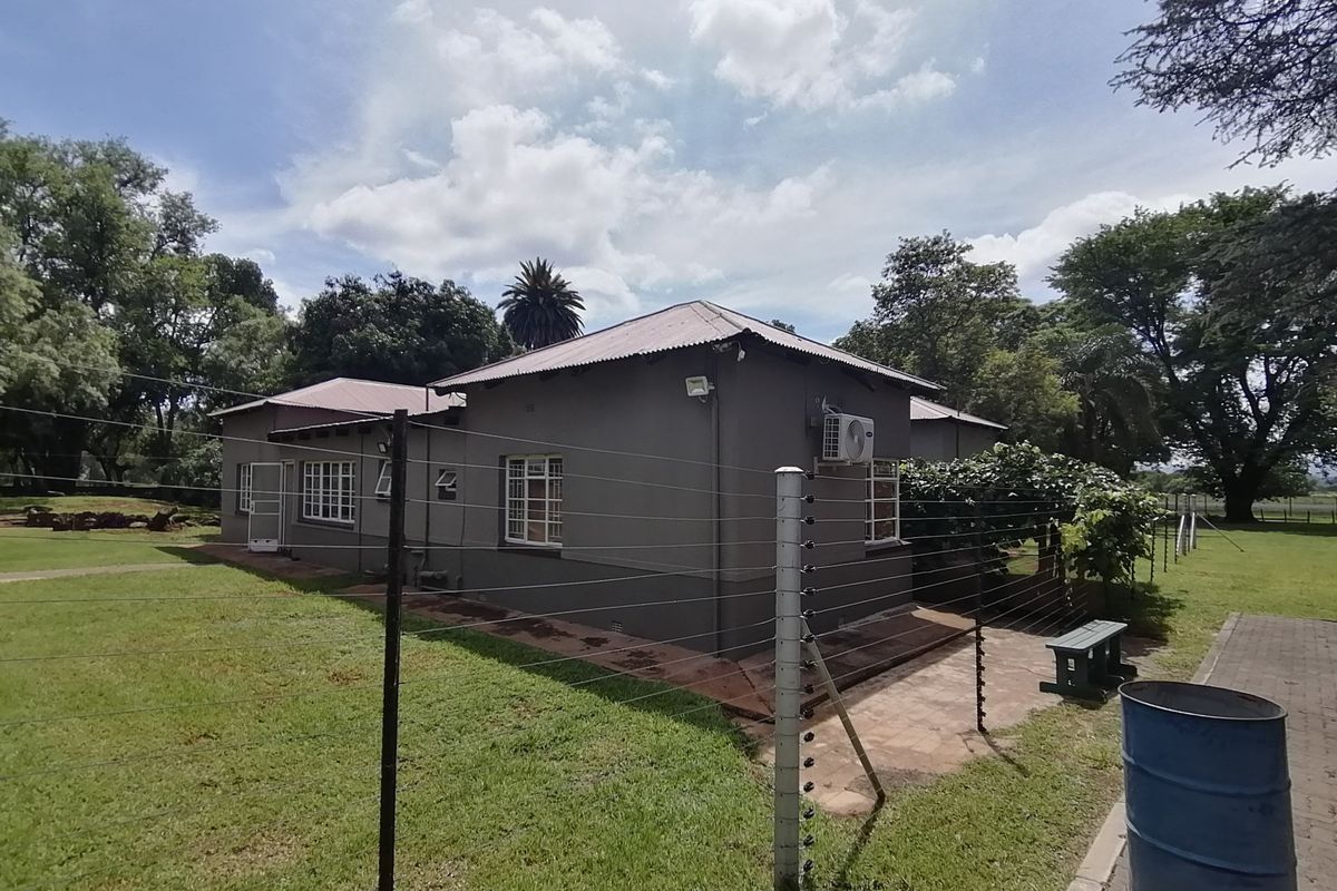 Rear view of the property featuring a corrugated metal roof, paved walkway, and perimeter electric fencing set within a spacious garden area.