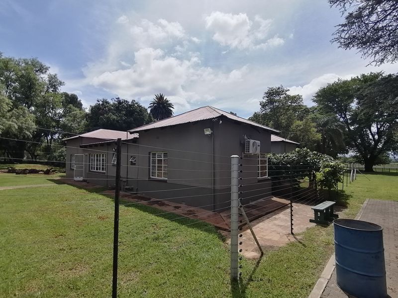 Rear view of the property featuring a corrugated metal roof, paved walkway, and perimeter electric fencing set within a spacious garden area.