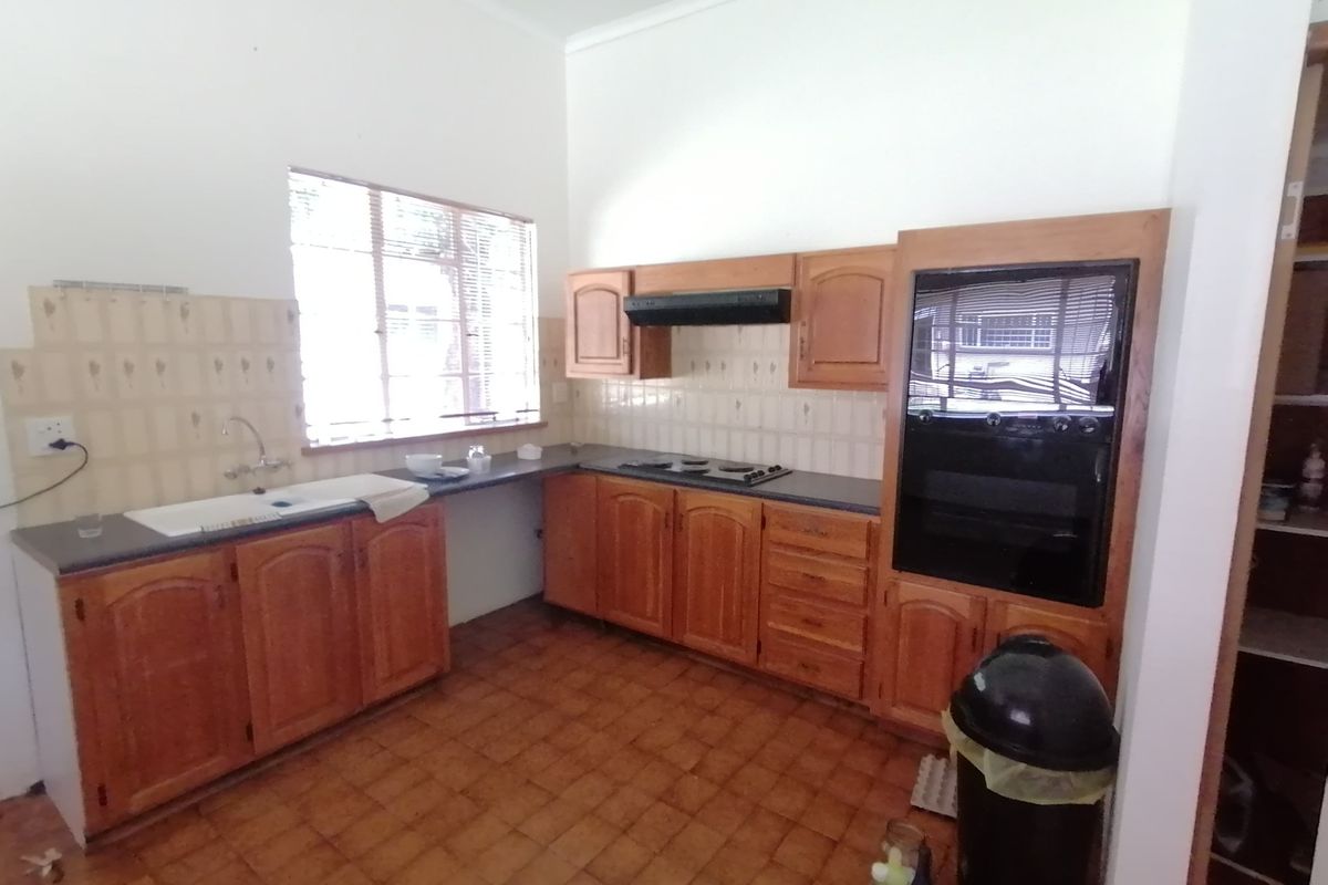 A functional kitchen featuring wooden cabinetry, built-in oven, hob, extractor fan, and tiled splashback with ample counter space.