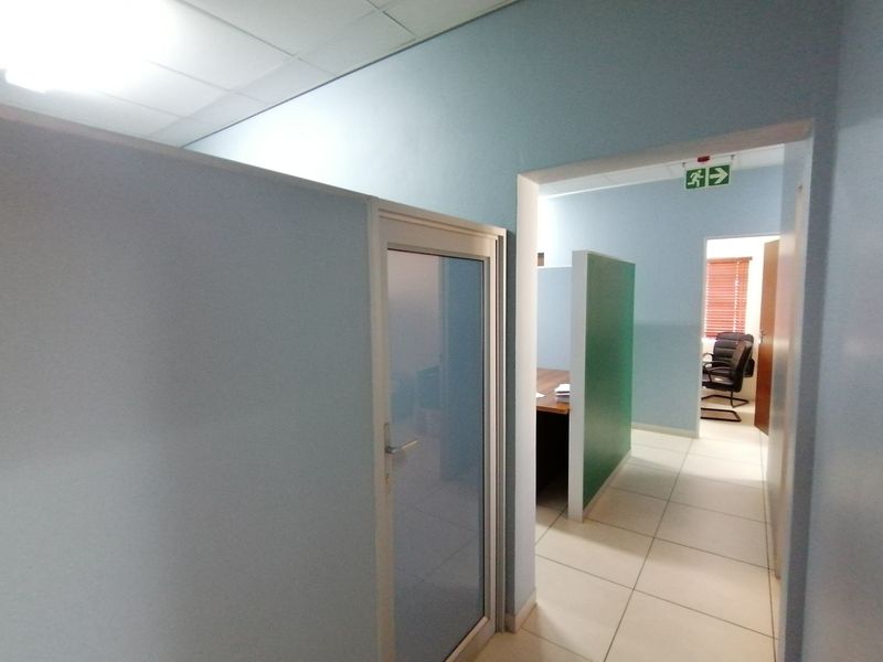 An office space featuring partition walls, tiled flooring, and a suspended ceiling with an emergency exit sign.