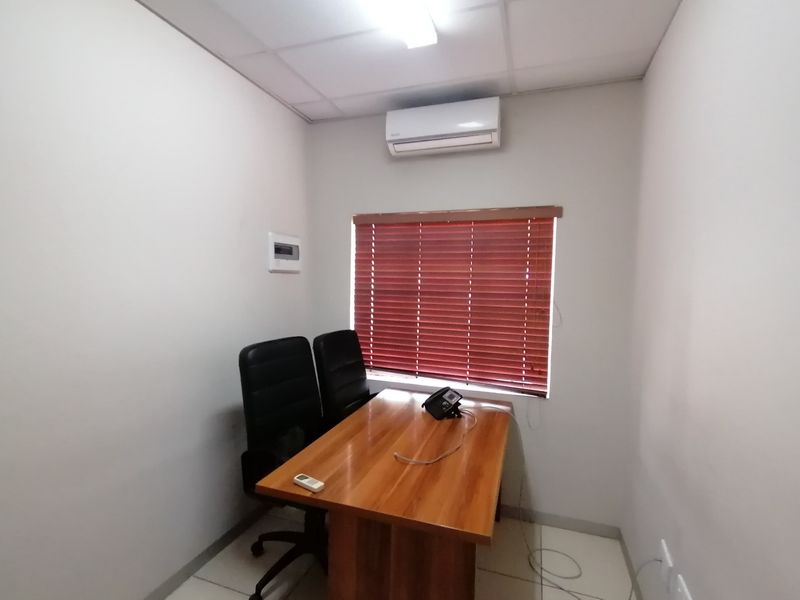 A functional office space featuring a split-system air conditioner, tiled flooring, and a window with fitted venetian blinds.