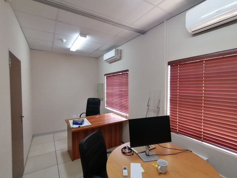 A functional office space featuring tiled flooring, suspended ceiling, dual split-system air conditioning units, and venetian blinds on the windows.
