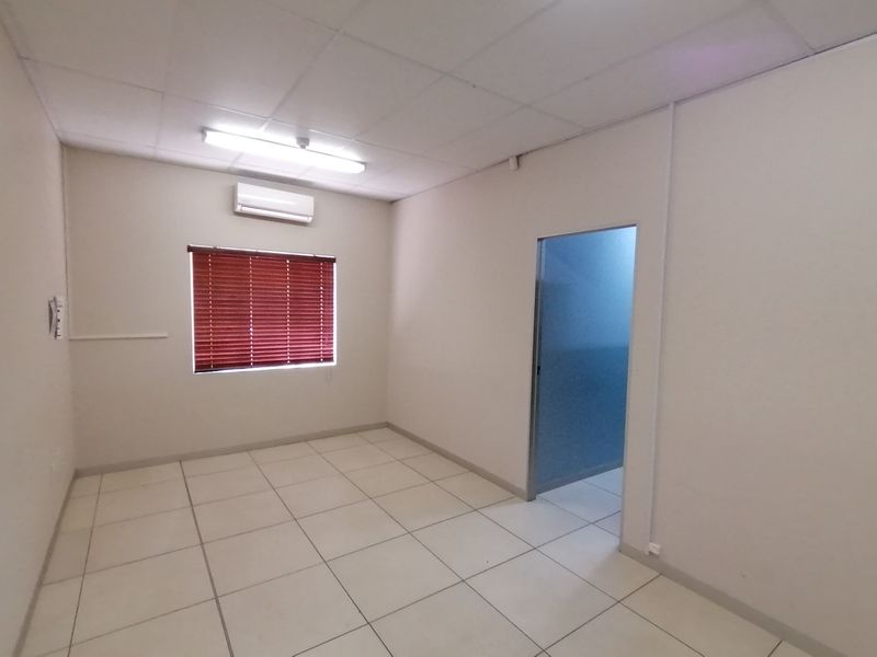 An empty, neutral-toned room featuring tiled flooring, a drop ceiling, and a wall-mounted air conditioning unit.