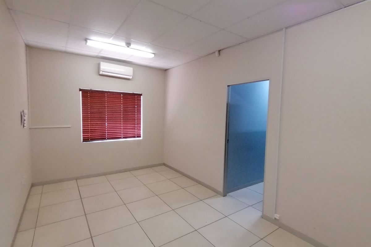 An empty, neutral-toned room featuring tiled flooring, a drop ceiling, and a wall-mounted air conditioning unit.