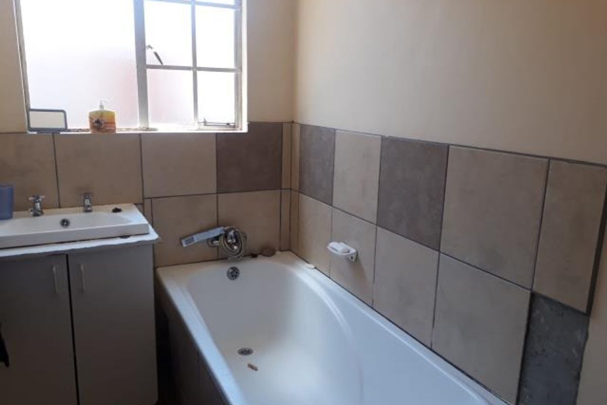 A functional bathroom featuring a bathtub, vanity cabinet with basin, and tiled splashback, currently showing signs of wear and missing wall tiles.