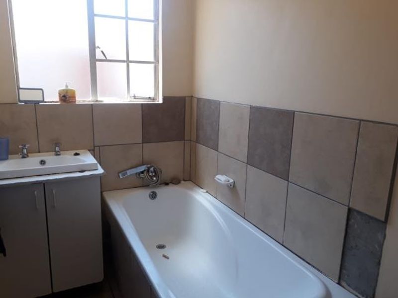 A functional bathroom featuring a bathtub, vanity cabinet with basin, and tiled splashback, currently showing signs of wear and missing wall tiles.