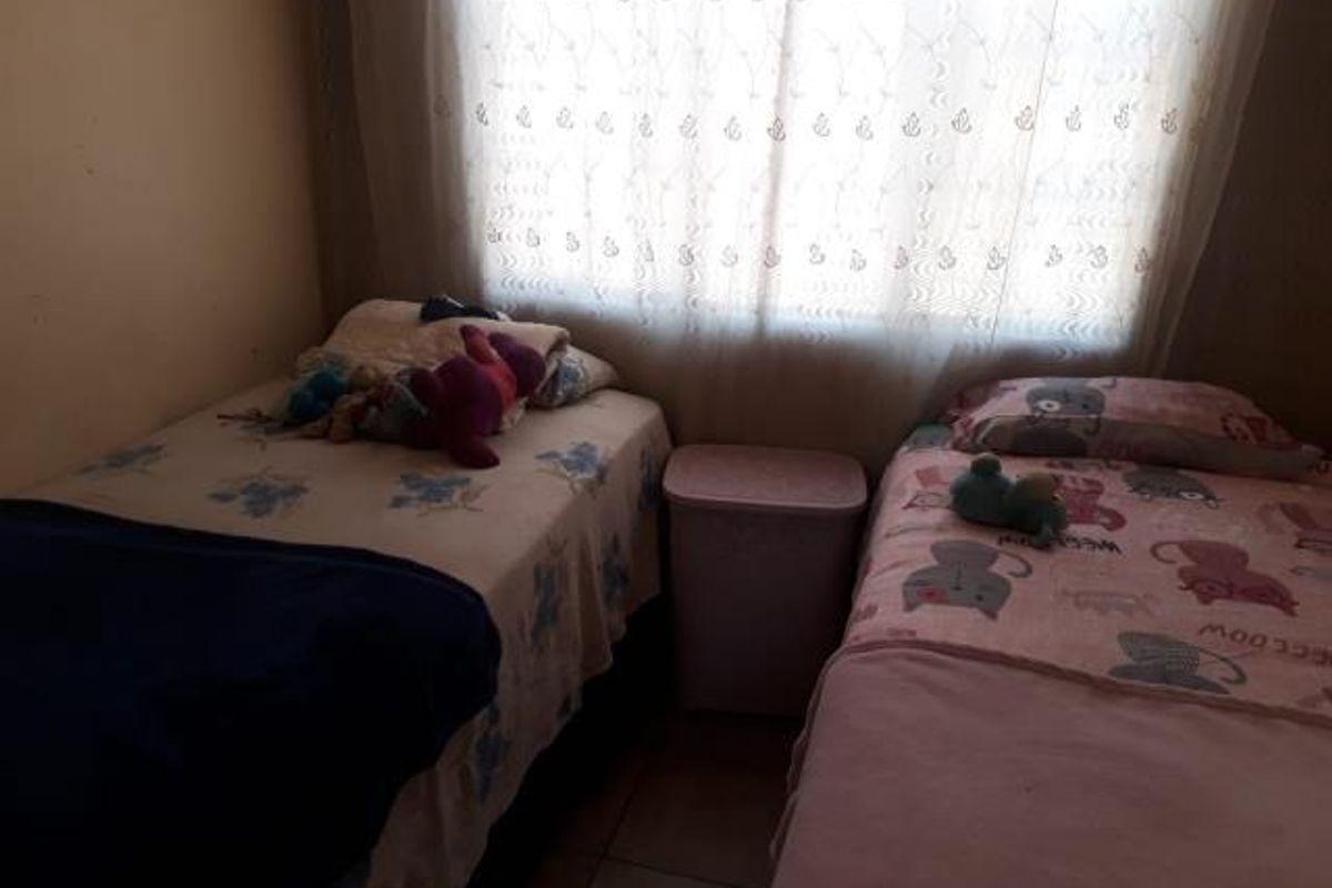 A functional bedroom featuring tiled flooring and a window with a curtain rail, providing a simple and practical living space.