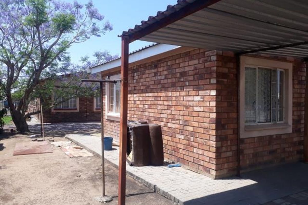 Exterior view of a face brick house featuring a metal carport, paved walkway, and established garden area.