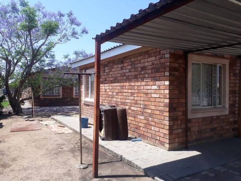 Exterior view of a face brick house featuring a metal carport, paved walkway, and established garden area.