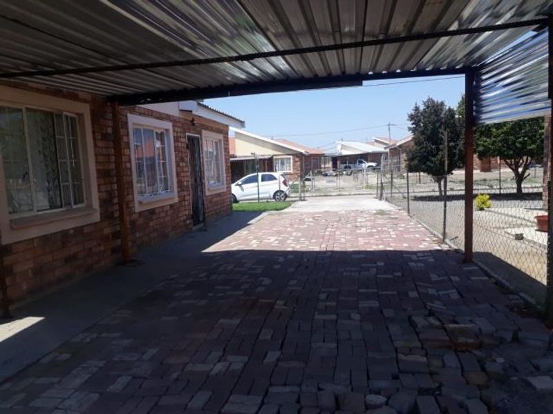 A covered outdoor patio area featuring a corrugated metal roof and brick paving, providing a functional space adjacent to the main house structure.