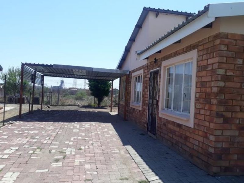 A side view of a brick house featuring a covered carport and a paved driveway area.