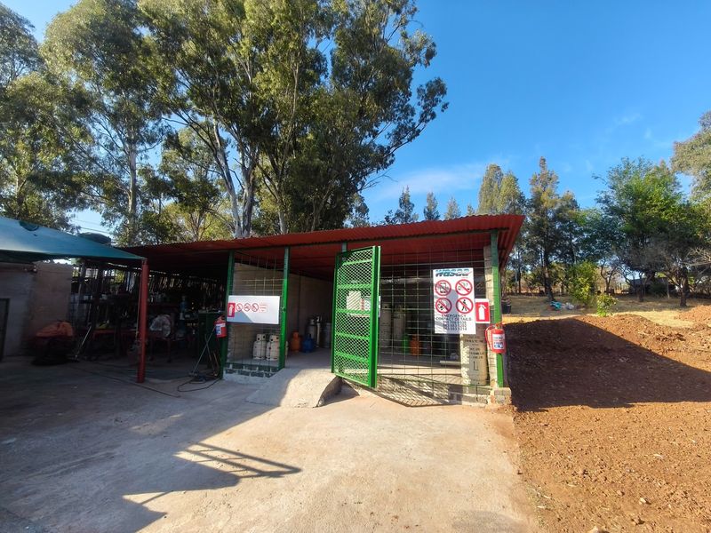A functional outdoor utility storage area featuring a corrugated metal roof, concrete ramp, and secure steel gate with safety signage and fire extinguishers.