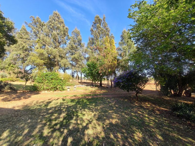 A spacious, well-maintained farm garden featuring mature trees, expansive lawn areas, and established perimeter fencing under a clear blue sky.