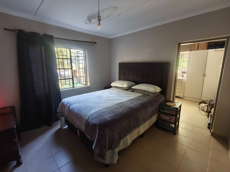 A bedroom featuring tiled flooring and security bars on the window, with visible ceiling damage requiring repair.