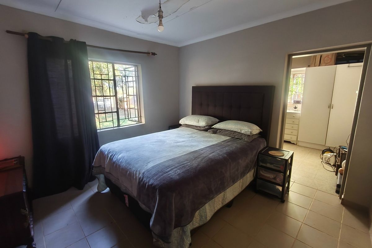 A bedroom featuring tiled flooring and security bars on the window, with visible ceiling damage requiring repair.