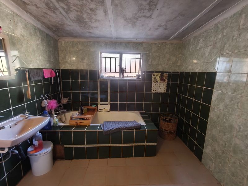 A dated bathroom featuring a built-in bathtub, wall-mounted basin, and dark green tiled walls. The ceiling shows signs of significant wear and staining.