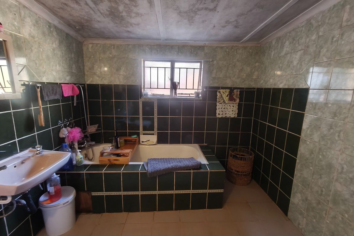 A dated bathroom featuring a built-in bathtub, wall-mounted basin, and dark green tiled walls. The ceiling shows signs of significant wear and staining.
